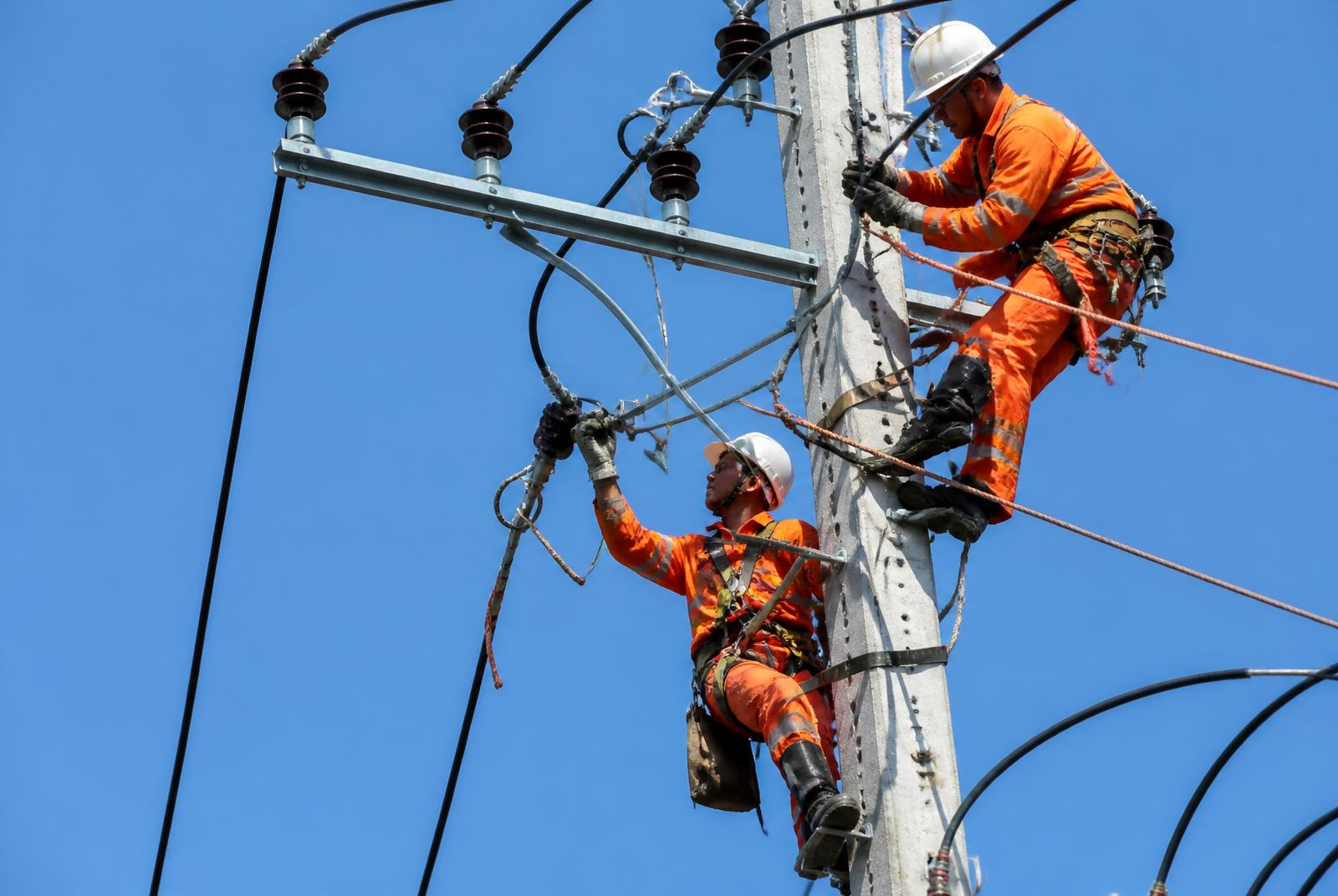 Two workers in hard hats on an overhead power line