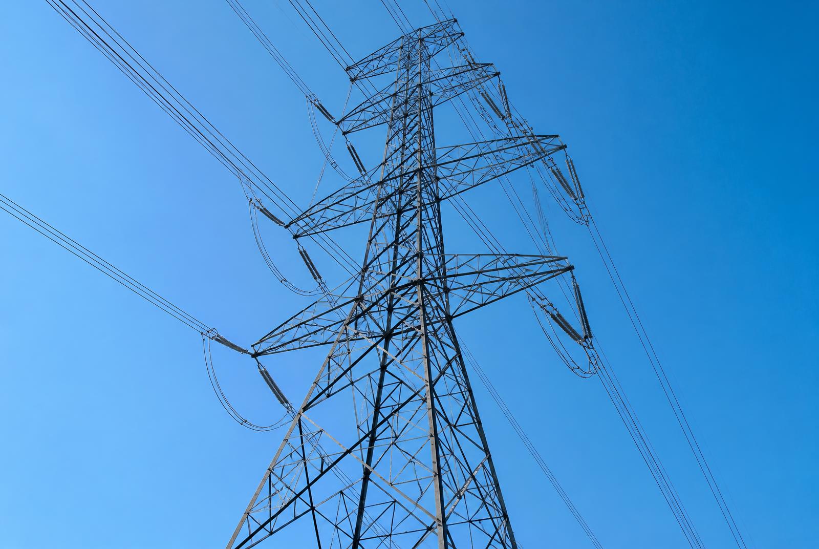 High voltage transmission tower against a bright blue sky